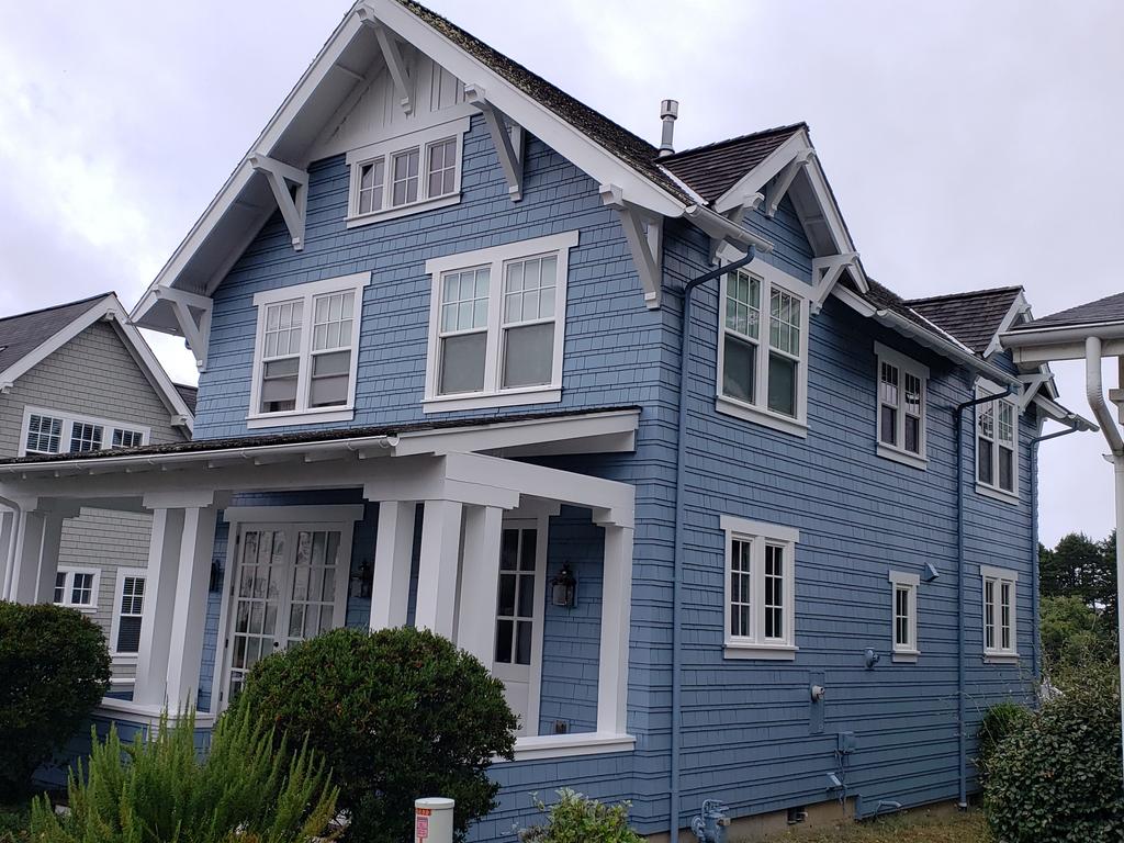 Blue two-story house with white trim and a covered porch on a cloudy day.