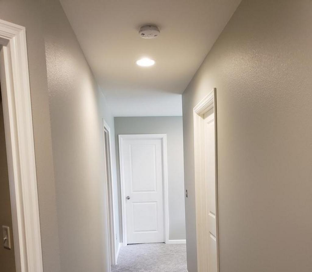 A narrow hallway inside a house with white walls and closed doors, illuminated by ceiling lights.