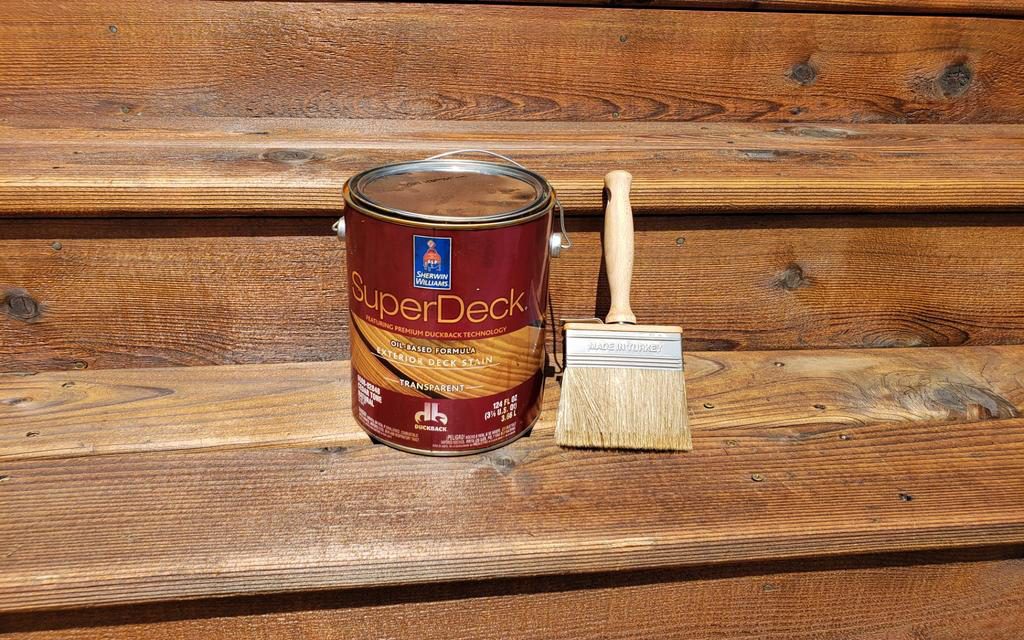 Can of superdeck stain with a paintbrush on a wooden surface.
