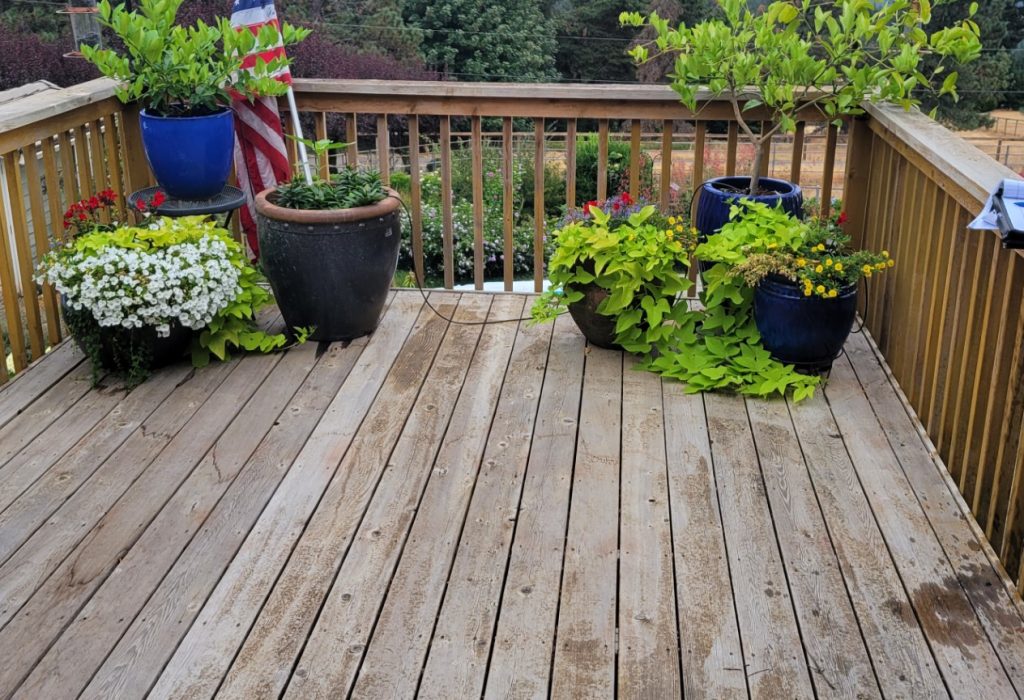 A wooden deck adorned with pots of lush green plants and flowers, against a backdrop of a hazy landscape.