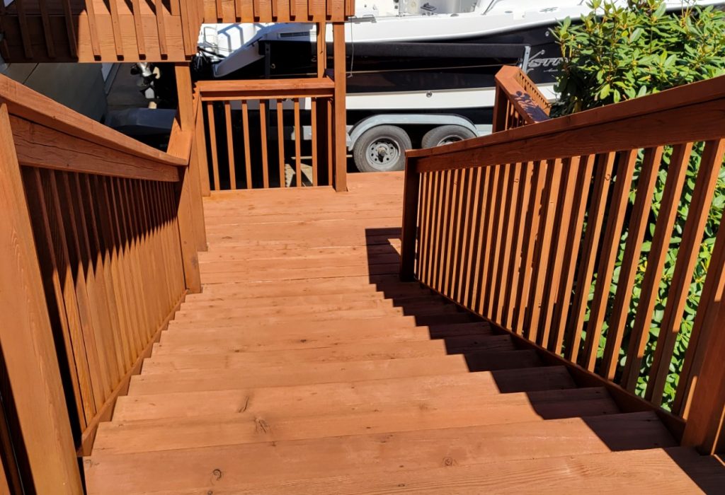 Wooden staircase leading down to a sunny outdoor area with a parked boat in the background.