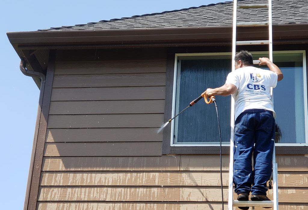 A person pressure washing the exterior siding of a house.